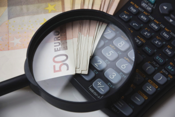A magnifying glass over euro banknotes and a calculator, symbolizing financial analysis and maximizing IT investment returns.