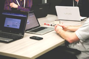 Three professionals sitting with laptops, discussing technology solutions, representing the comparison between in-house hiring and subscription-based architecture services.